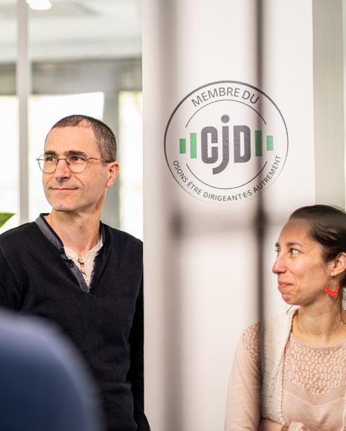 Groupe de collaborateurs en pleine discussion dans un cadre professionnel, avec un badge du CJD affiché en arrière-plan.